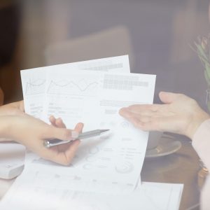 Close-up of two businesswomen sitting at the table pointing at financial documents and discussing it together during meeting