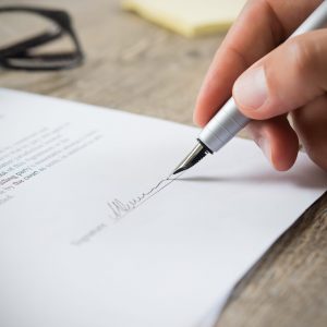 Close up of hand of businessman signing a form. Business man signing contract for future deal. Business man signing legal document. Male hand signing employee contract with a bond.